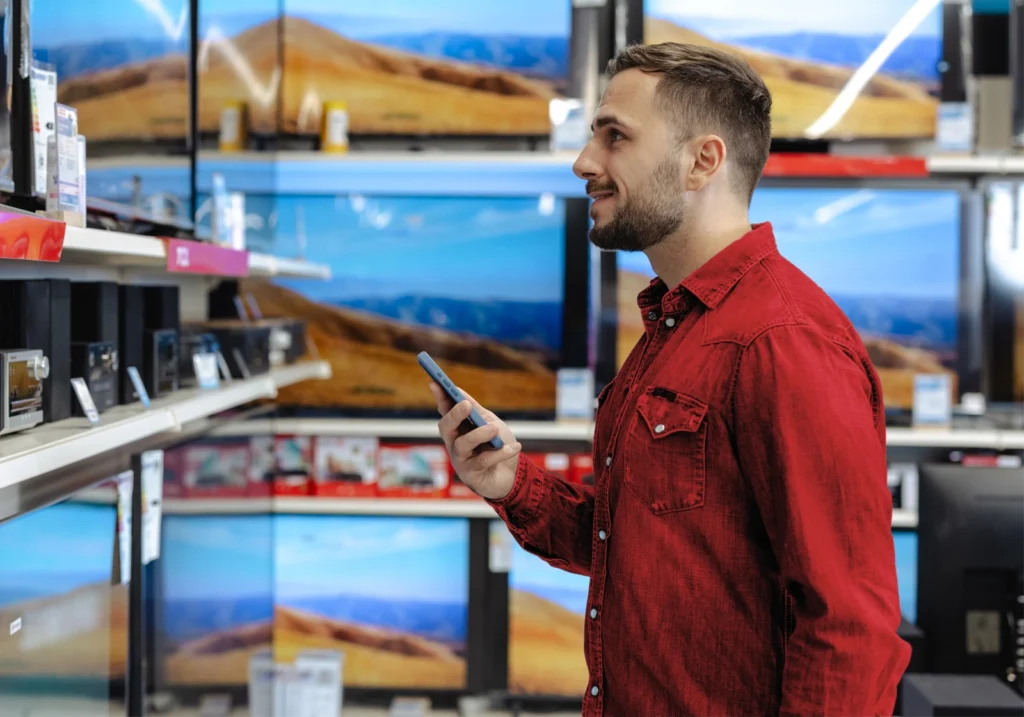 Smiling man in an electronics store feeling confident about his next purchase after improving his spending habits.
