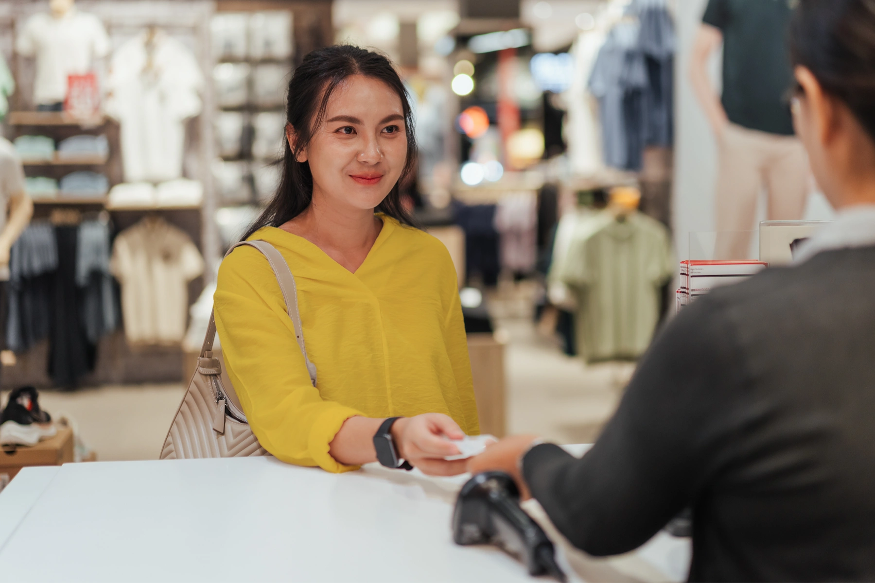 Young woman hands her debit card to a cashier for an in-store purchase.