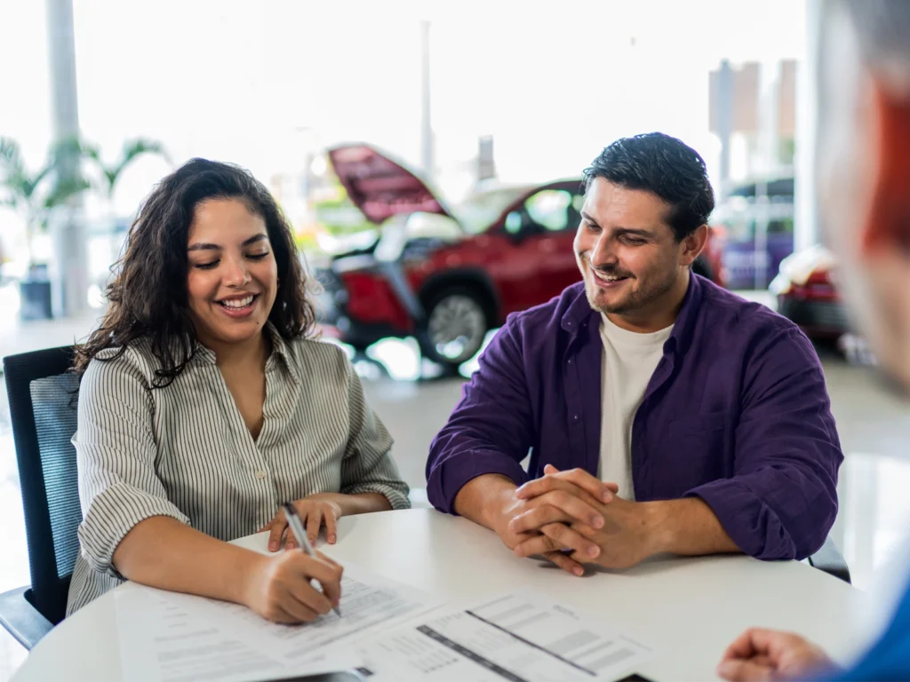 A smiling borrower confidently completes a credit application at a car dealership after boosting her 5 C’s of credit.