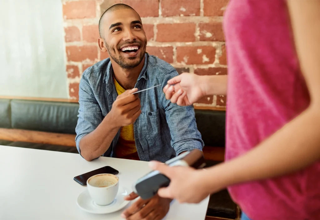 A man hands his debit card to a server in a cafe.