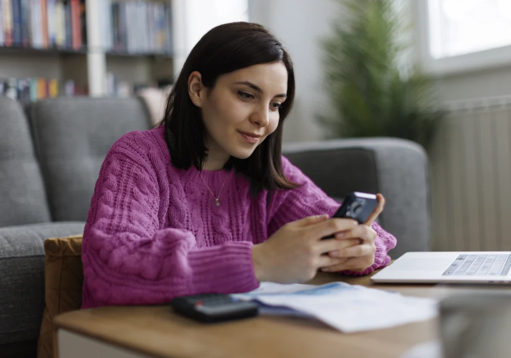A smiling woman reviews her monthly budgeting checklist and spending plan on her smartphone.