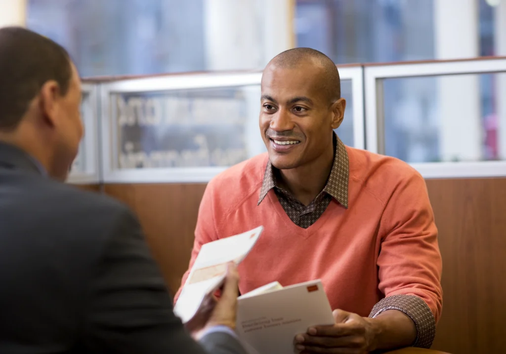 A man meets with a banker at a local branch to discuss account details and associated bank fees.