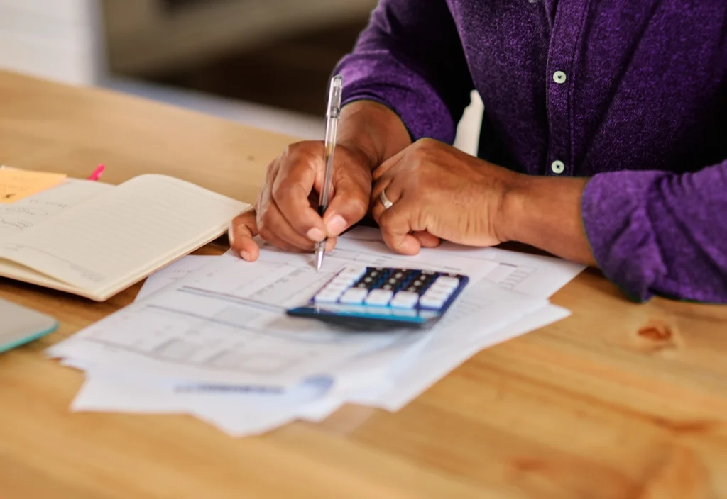 A person uses a calculator, pen, and paper to calculate debt payoff.