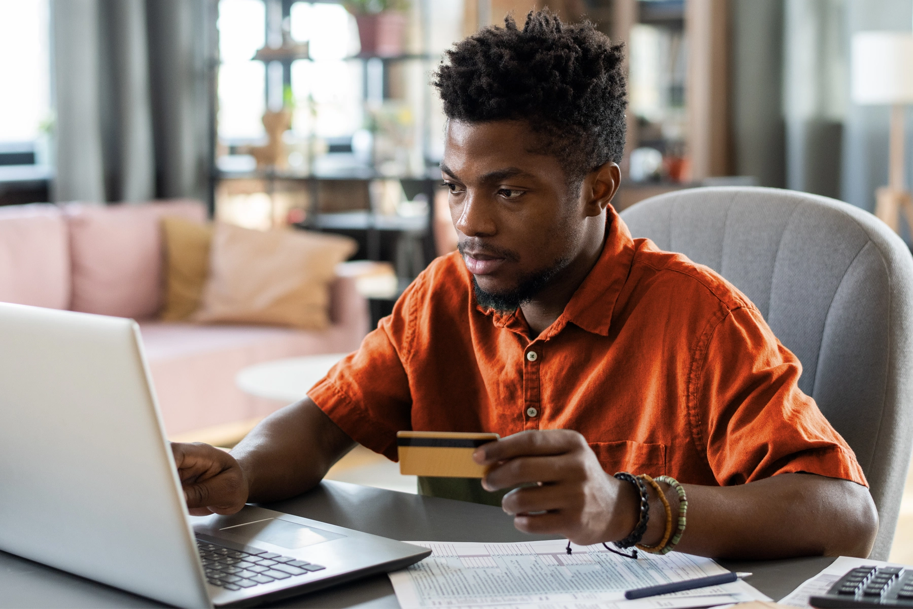 A young man holds a credit card in one hand and uses a laptop with the other.