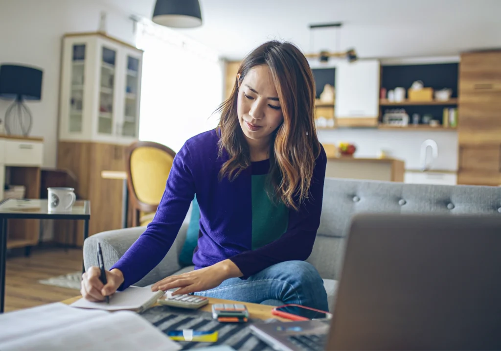 A woman sits on her couch creating a financial plan for when financial emergencies happen.
