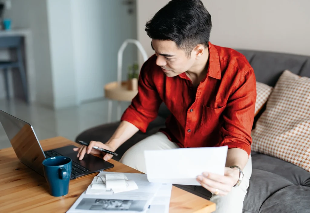 Man keeps record of his gig work income and expenses on his laptop while sitting on his couch.