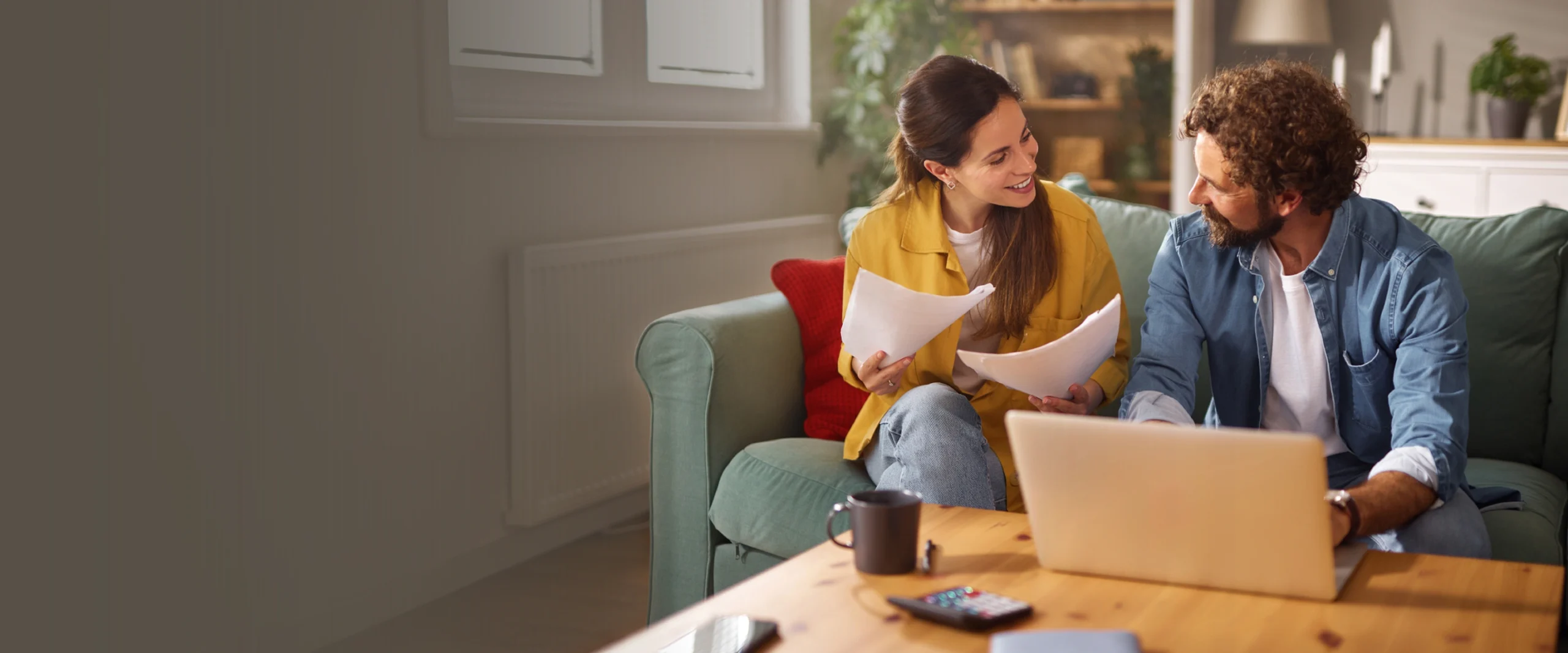 Young couple sits together on their couch, reviewing their financial situation and exploring ways to combine finances.