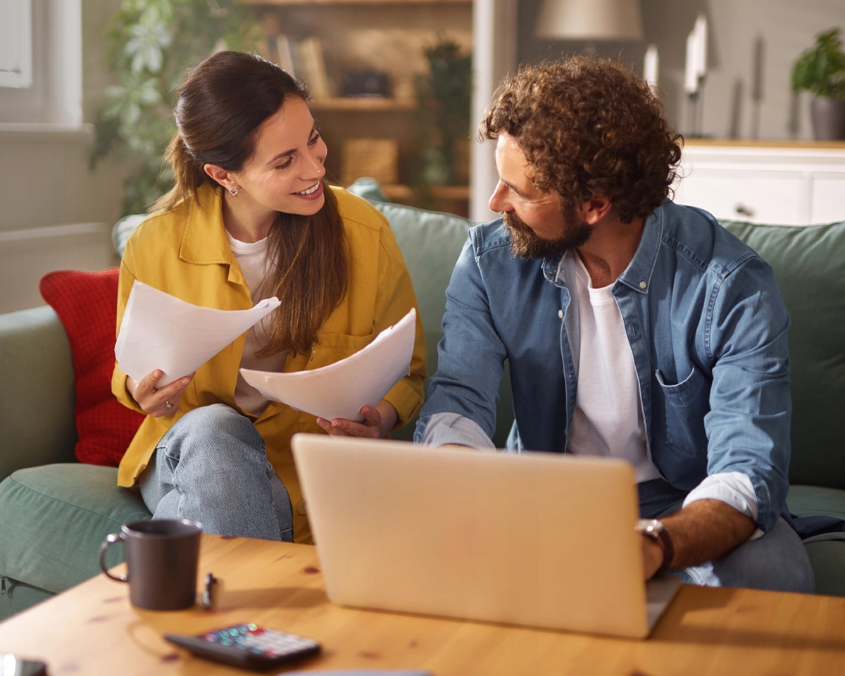Young couple sits together on their couch, reviewing their financial situation and exploring ways to combine finances.
