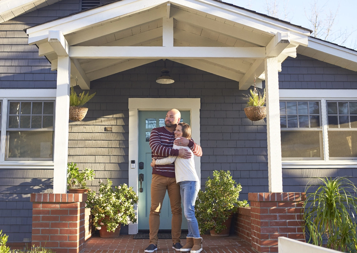 An adult and child stand together outside a home.