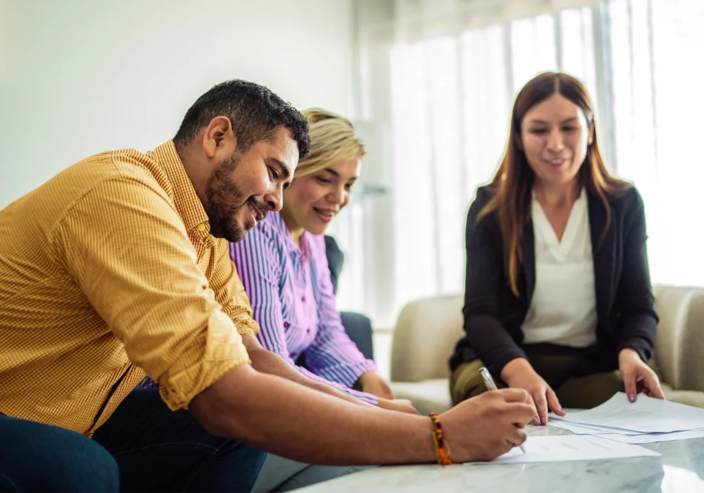Couple sits on a couch and completes paperwork related to their home loan in the presence of a loan officer.