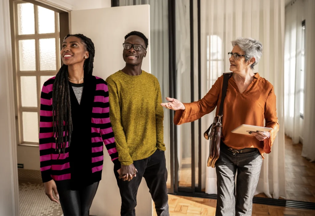 A real estate agent gives a smiling couple a house tour and gives them details on the home loan process.