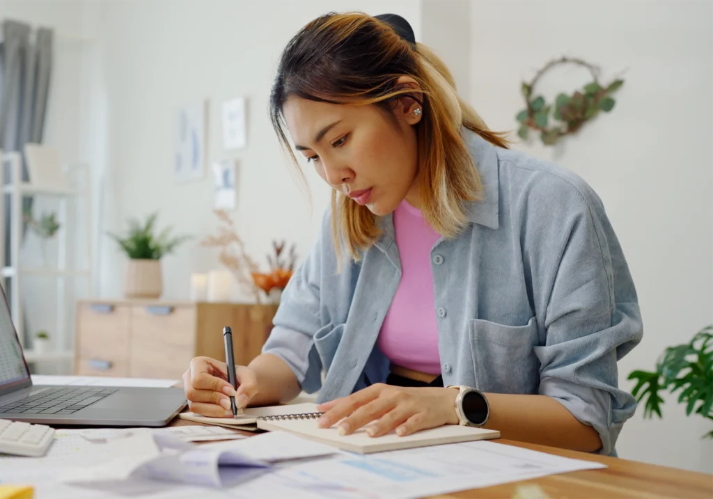 A woman writes down figures on paper as she works to manage her debt.