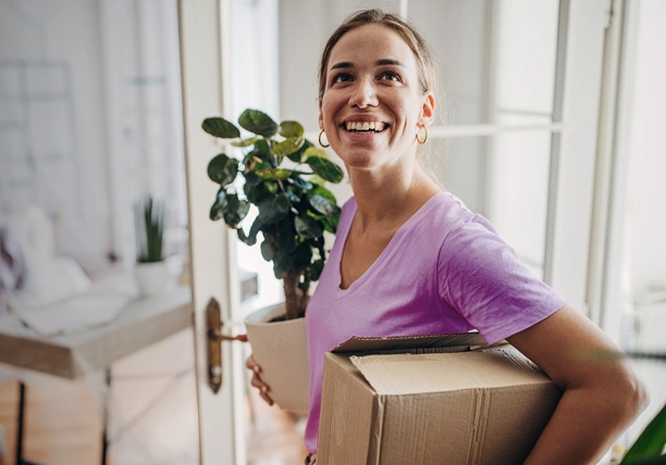 A woman carries a plant and a box into her new residence.