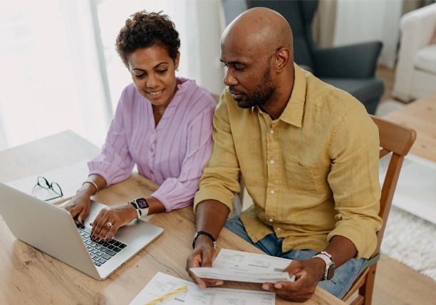 A couple uses pen, paper, and a laptop to assess their financial goals.