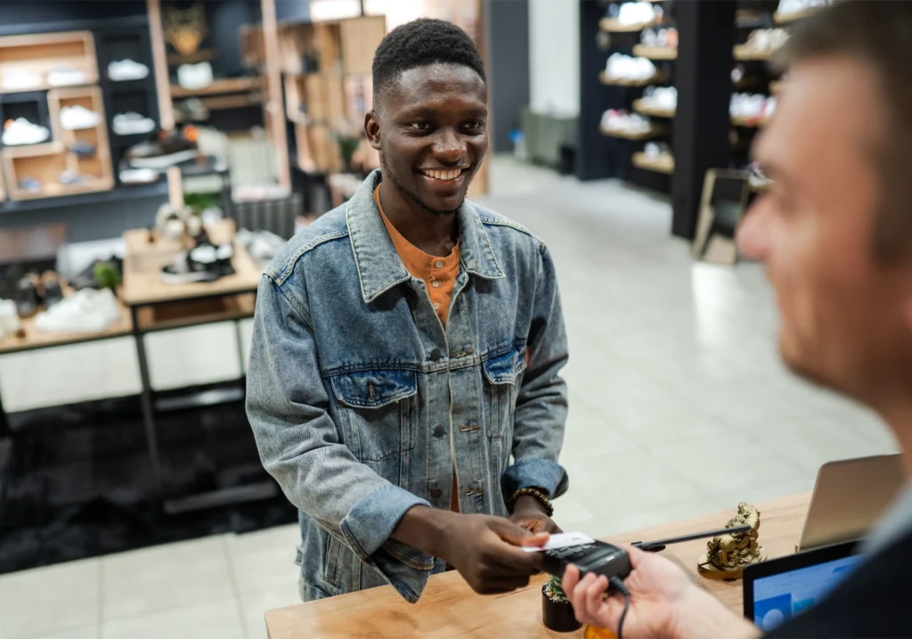 Smiling young man hands his credit card to a cashier in a shoe store.