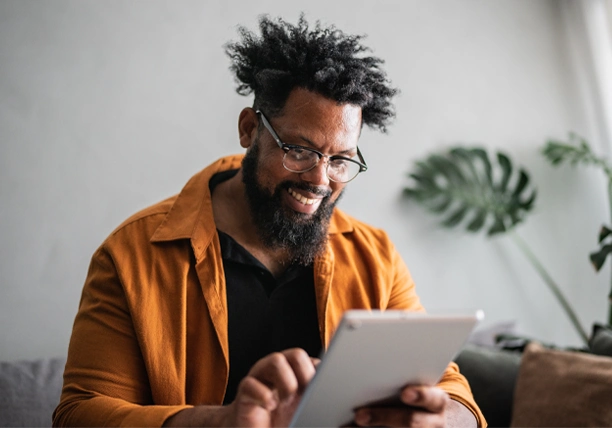 A man sits in his home and uses a tablet to review his monthly cash flow.