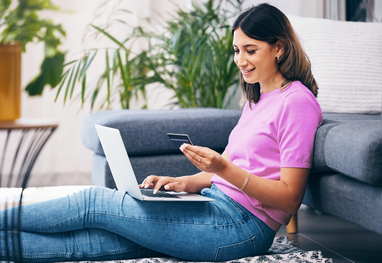 Young woman sits on the floor in front of her couch, researching common credit card features.