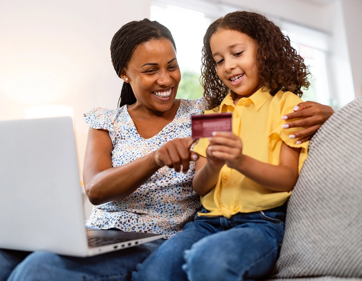 Adult helping a child learn about money with a card and laptop.